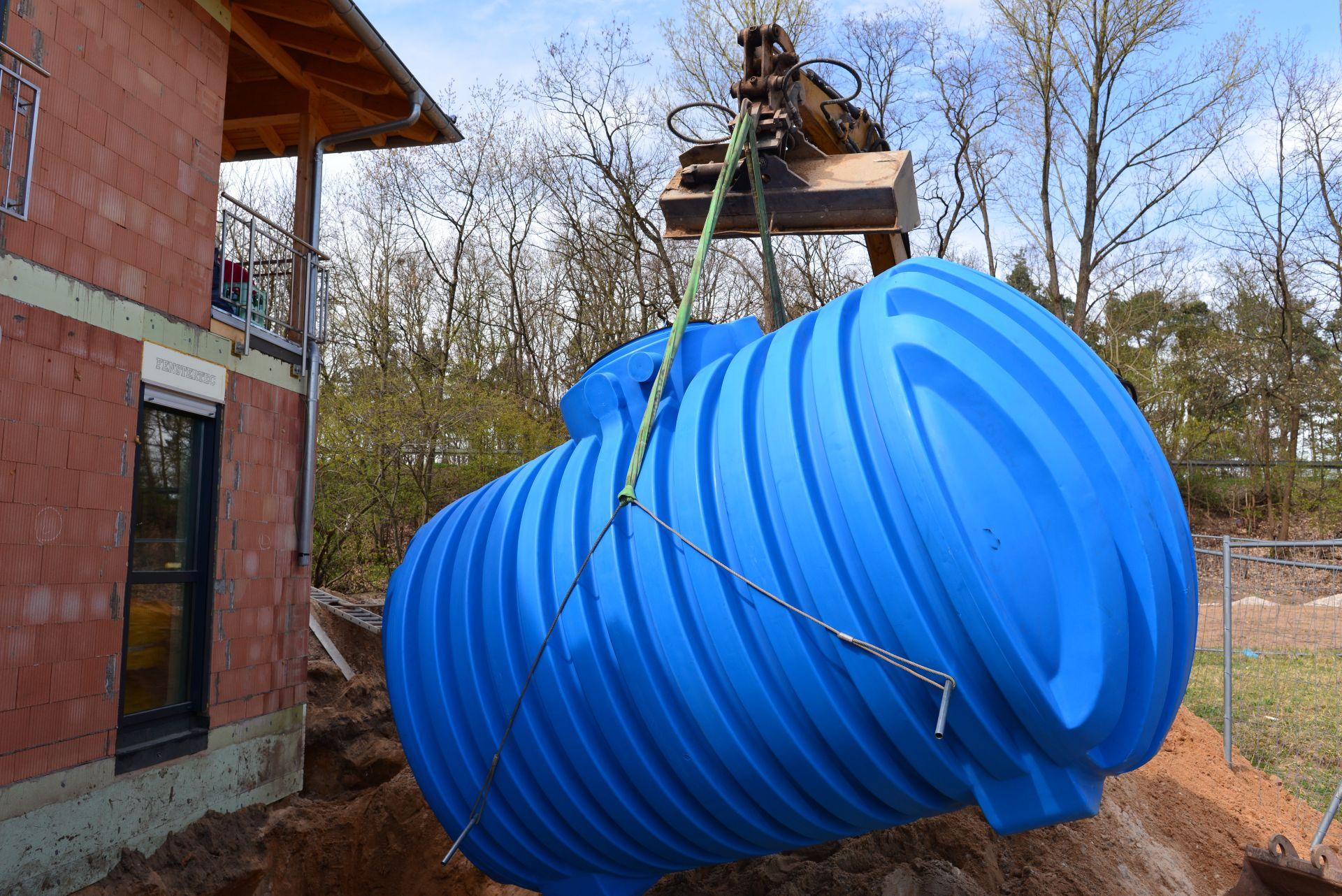 Einbau einer großen blauen Kunststoffzisterne mit Kran neben einem Einfamilienhaus im Rohbau