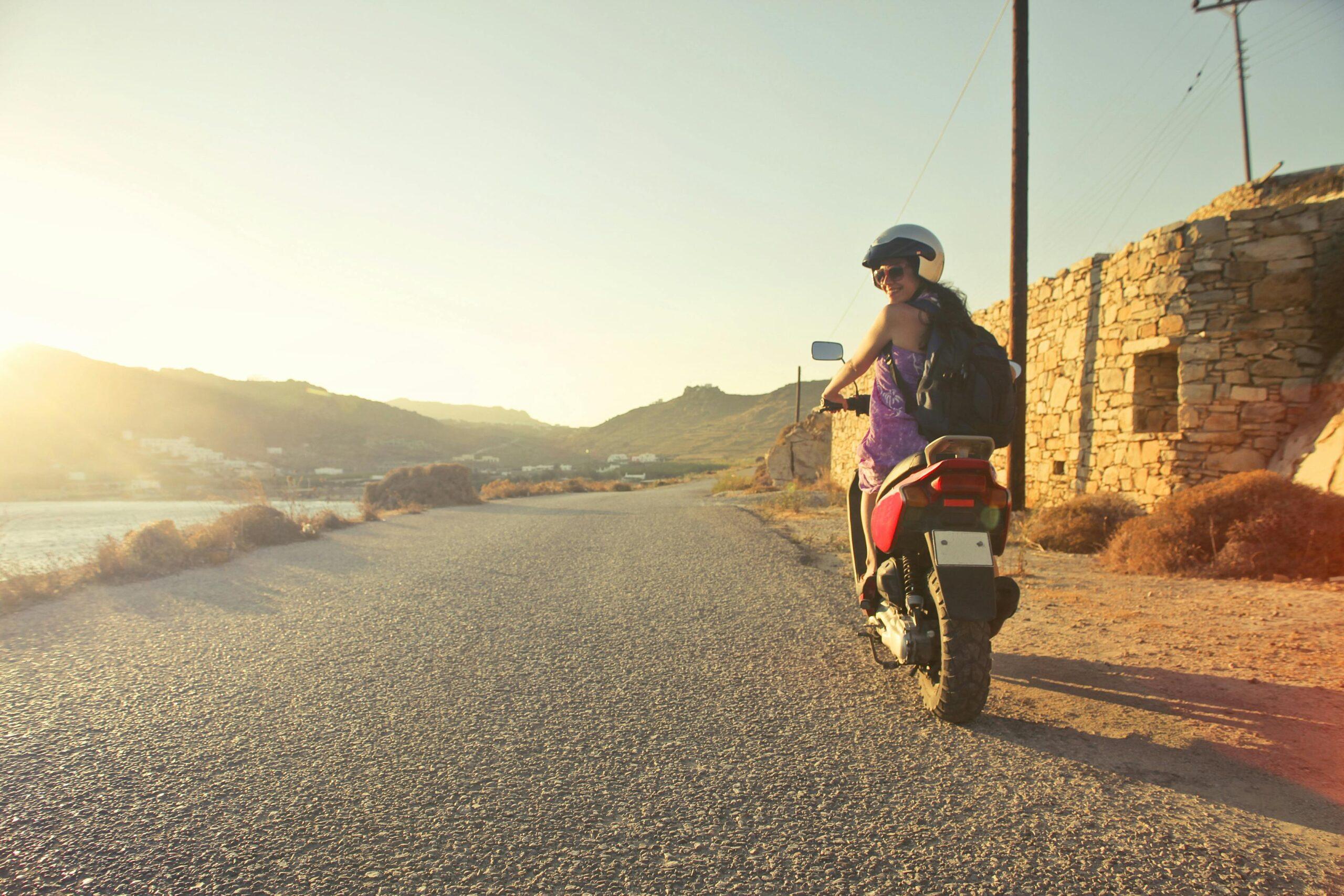 Eine Fahrerin genießt eine Ausfahrt im Sonnenuntergang auf ihrem 50ccm Motorrad auf einer ruhigen Landstraße mit Blick auf die hügelige Landschaft