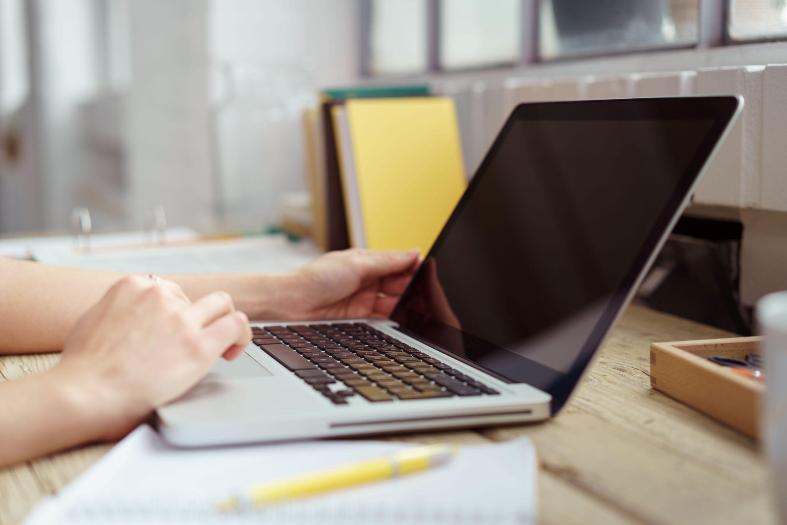 Eine Person sitzt an einem Laptop und arbeitet damit 